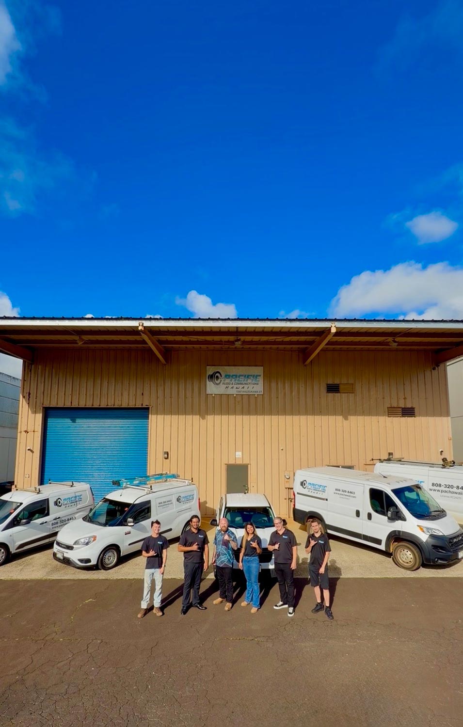 Six employees standing before a warehouse with a blue garage door and white work vehicles