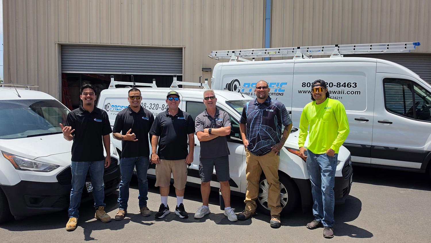 Six men standing proudly in front of parked white work vehicles on a sunny day