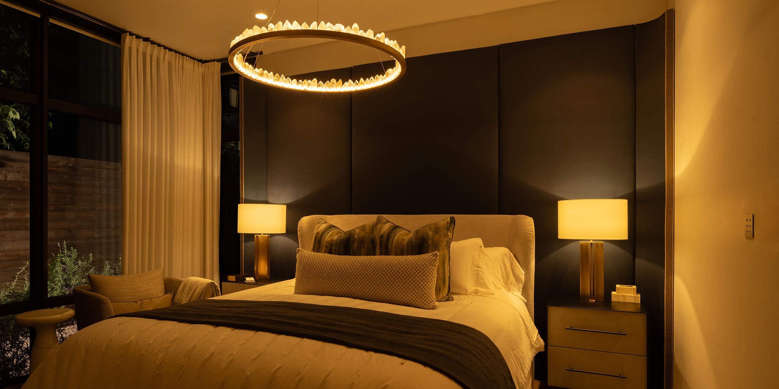Warmly lit bedroom with modern chandelier and dark accent wall