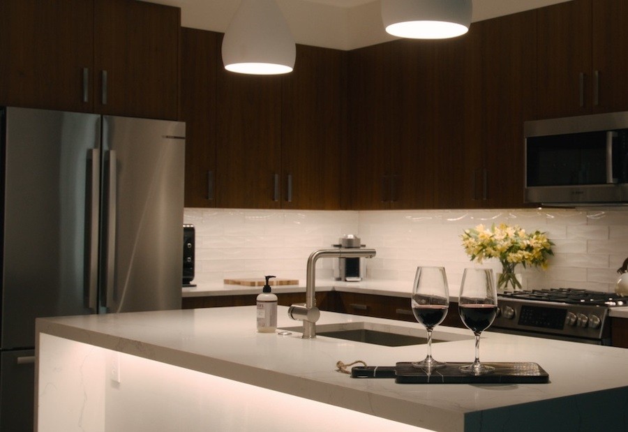 A well-lit modern kitchen with stainless steel countertops and fridge with two glasses of red wine on the center island.