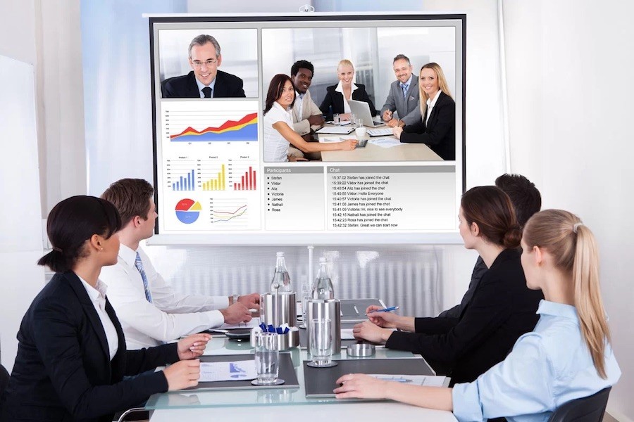 people sitting around a conference table looking at charts and virtual meeting attendees on a large screen