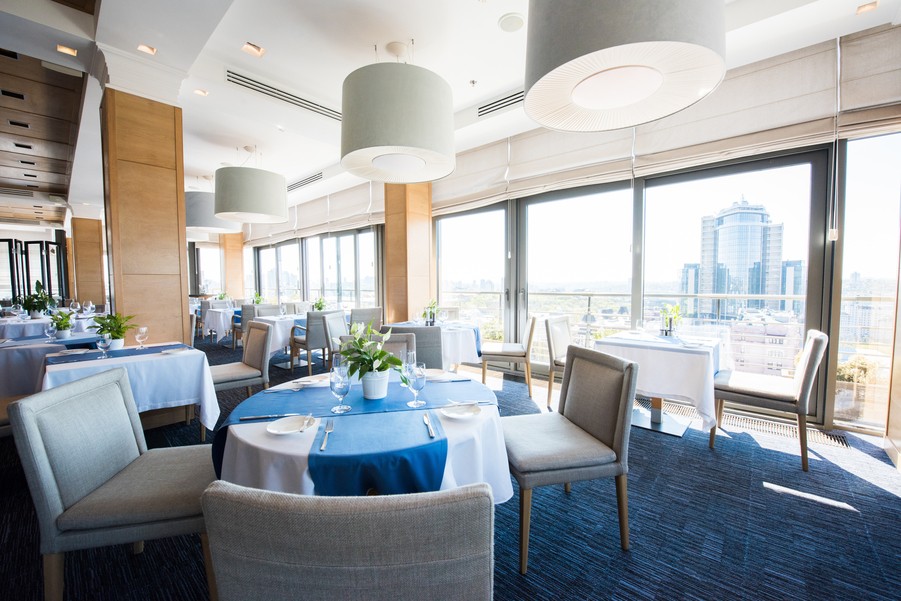 A restaurant with a blue and white color scheme, with floor-to-ceiling windows that oversee the city. 