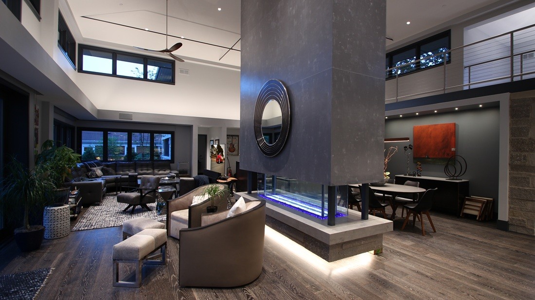 Open-concept living space features a double-sided fireplace with ambient lighting, contemporary furnishings, and expansive windows that frame the outdoor view.