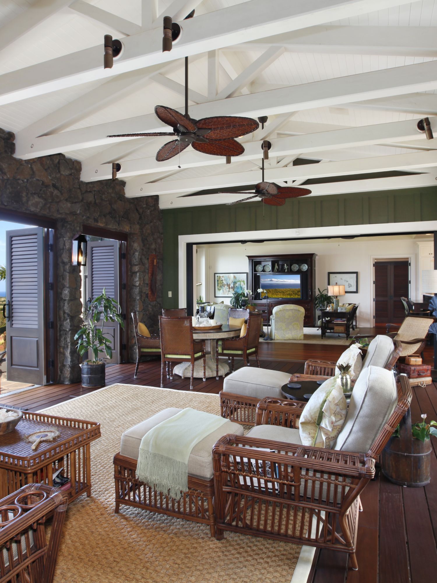 Open living area with wicker furniture, wood beams, and ocean view through open doors