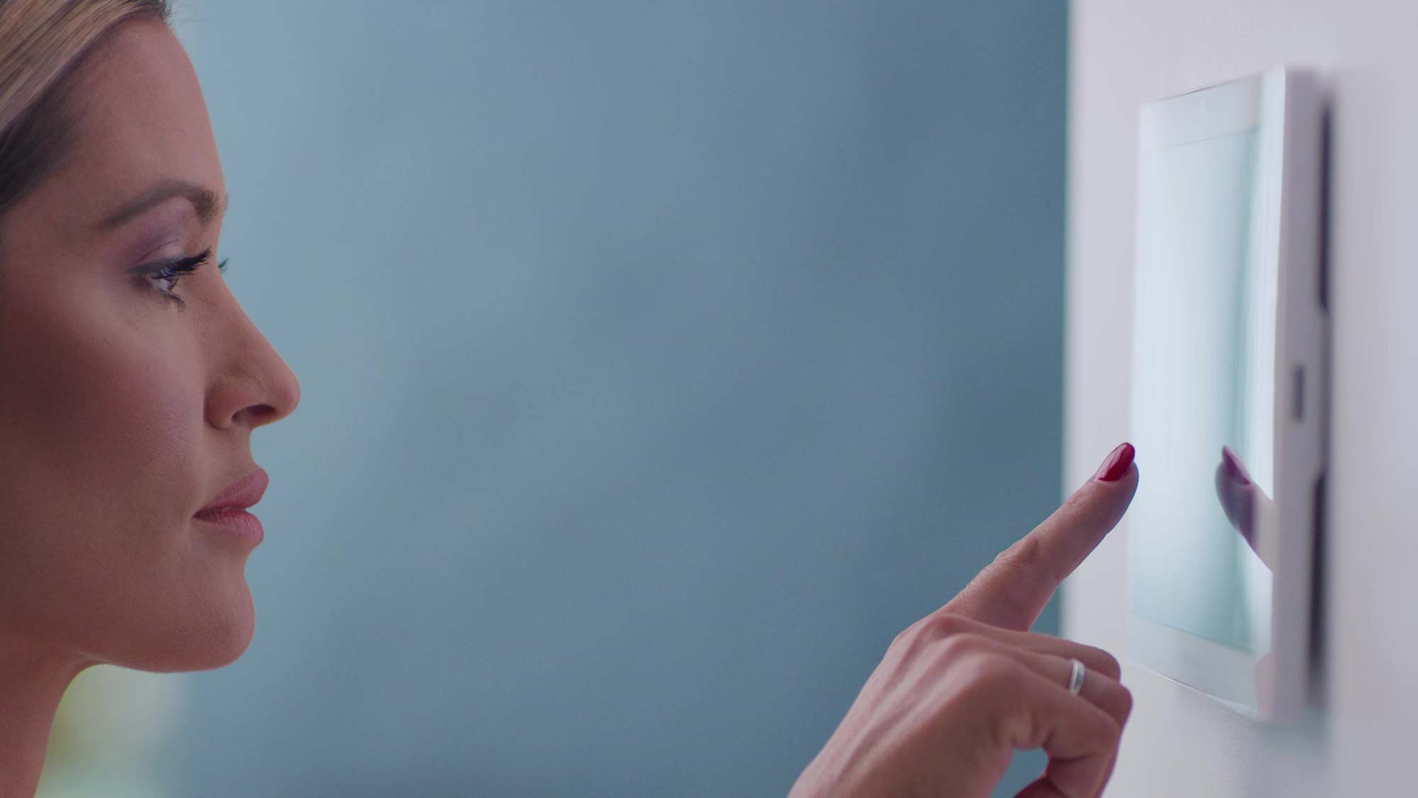 A woman using a modern touchscreen panel to control a smart lighting system.